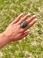 Hand wearing a large ring with a turquoise stone against a grassy background