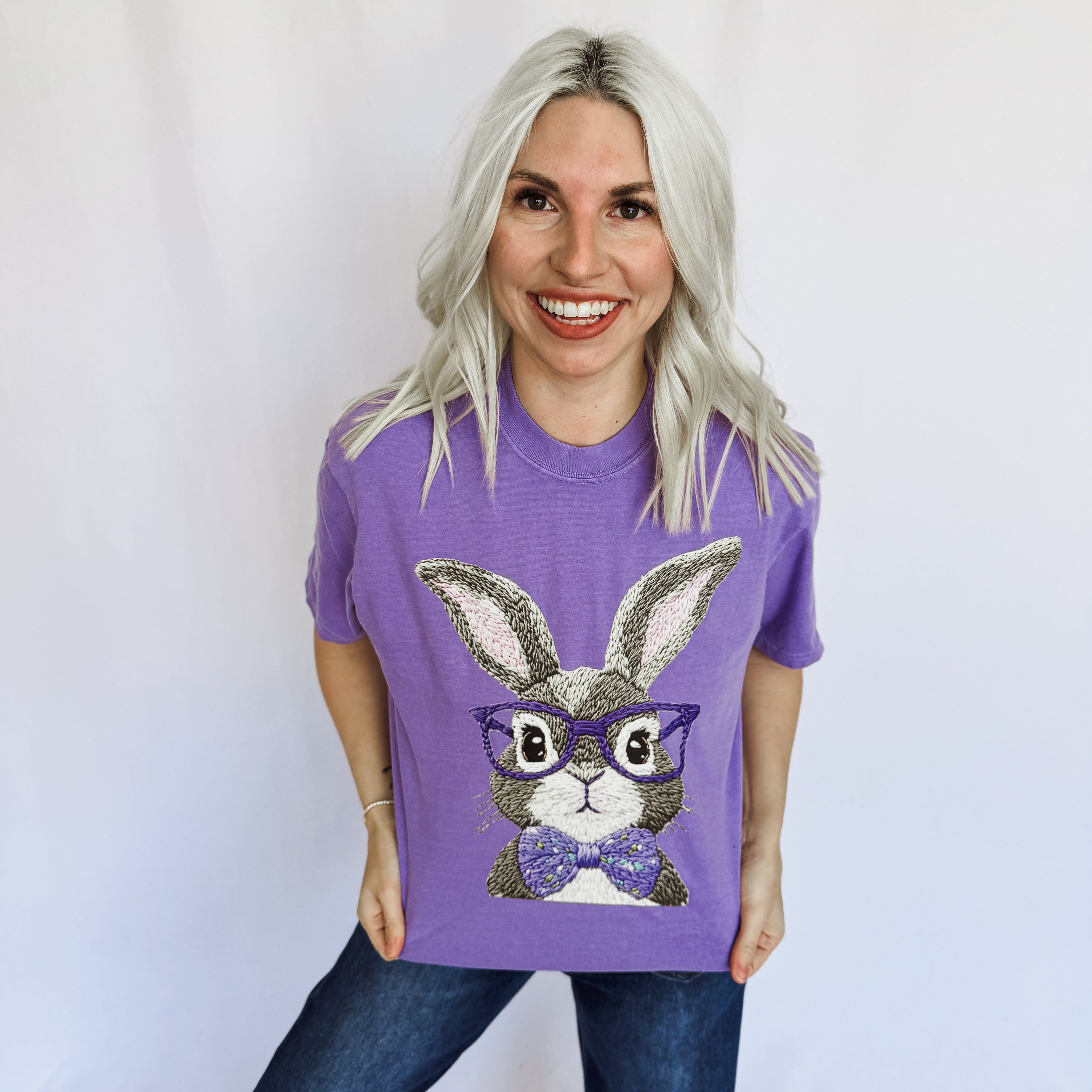 Woman wearing a purple t-shirt with a bunny graphic and glasses on a plain background