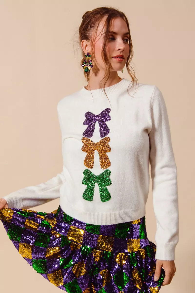 Ivory Mardi Gras sweater with sequin embellishments and decorative bow ribbons in purple, gold, and green, knit fabric, crew neckline, long sleeves, relaxed fit