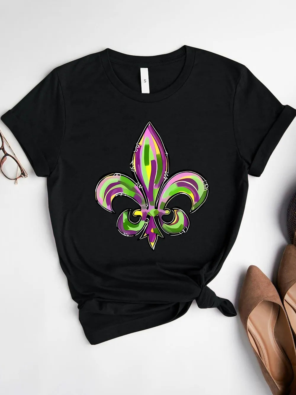 Black graphic tee with purple, green & gold fleur-de-lis Mardi Gras design. Soft stretch fit for parade season and everyday festive styling.