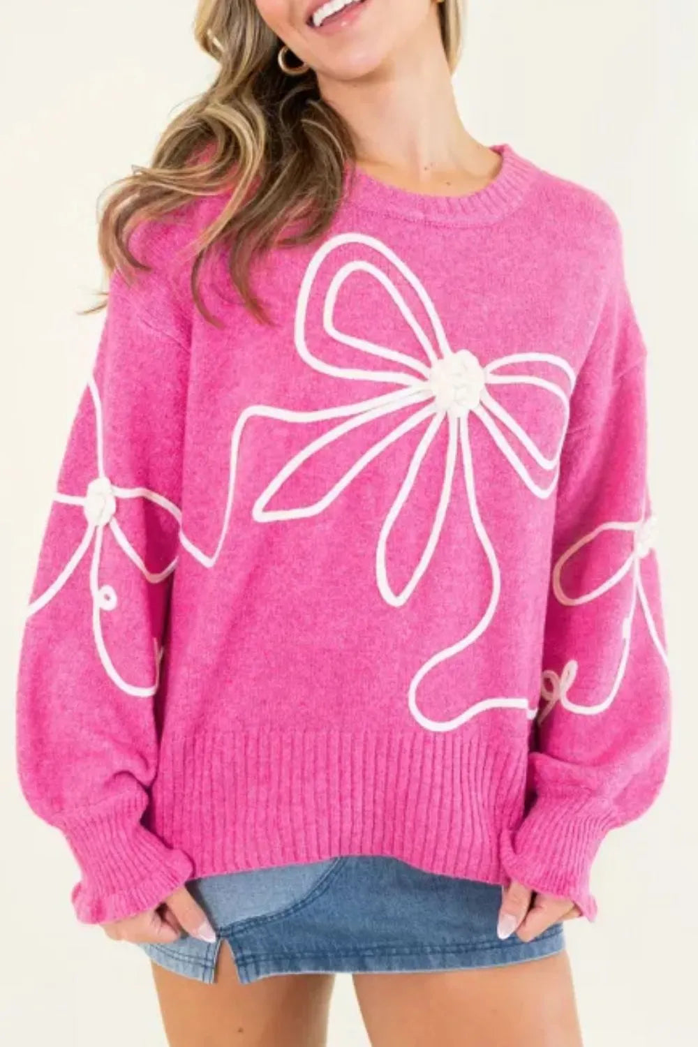 Pink knit pullover with white bow print, ribbed cuffs, and a relaxed dropped shoulder fit. Opaque fabric, cozy, casual, everyday favorite.
