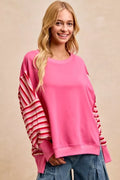Pink French terry pullover with soft striped sleeves and open-seam stitching. Relaxed fit, opaque fabric, casual everyday comfort top.