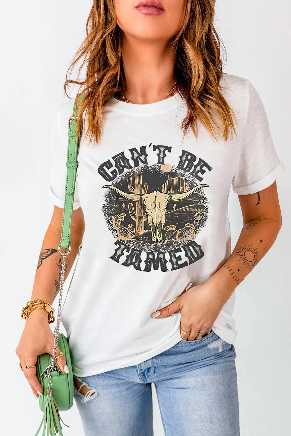 White western graphic tee with a “Can’t Be Tamed” skull leaned against an old barn. Neutral, bold, and perfect for denim, boots, and layered country outfits.
