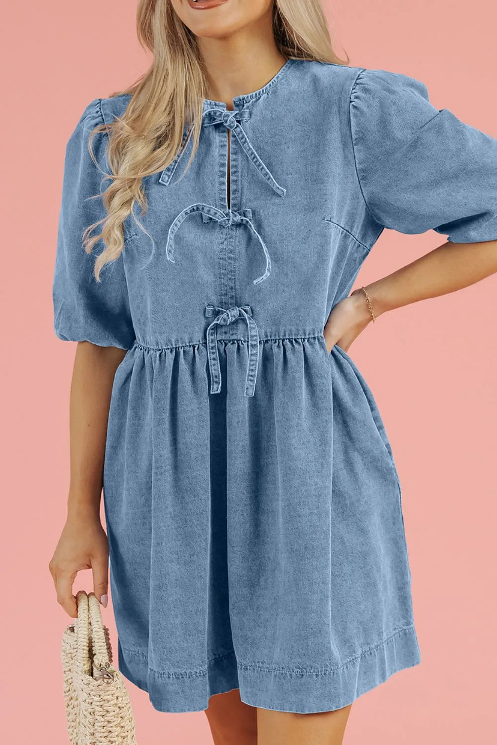 Above-knee denim dress with balloon sleeves, elastic cuffs, and a gathered waist. Soft gathered fit with a stitched bow accent and a flattering cinched silhouette.