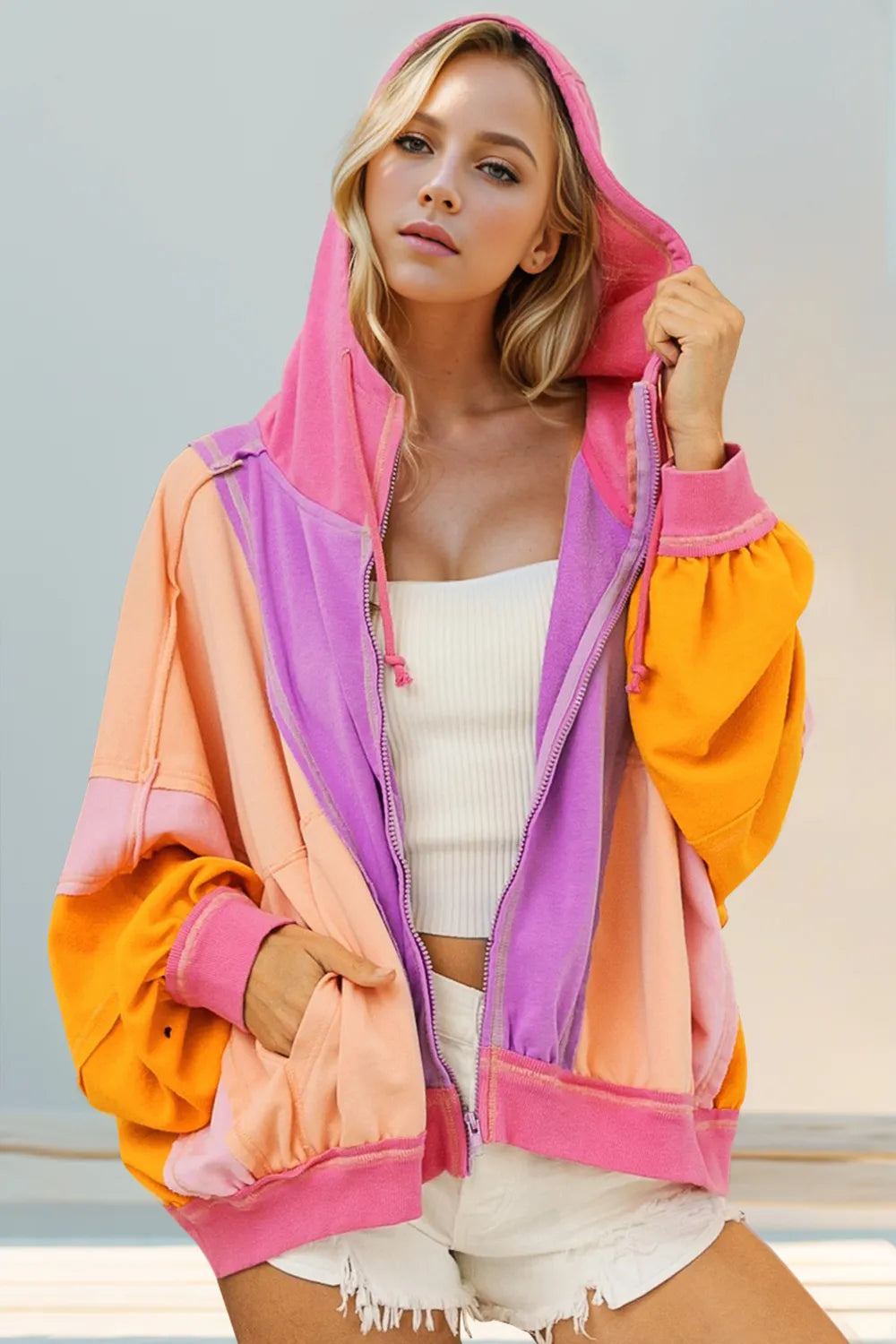 Purple hoodie with orange and pink color block accents. Zip up with pockets and exposed seams for a vibrant, cozy statement layer.