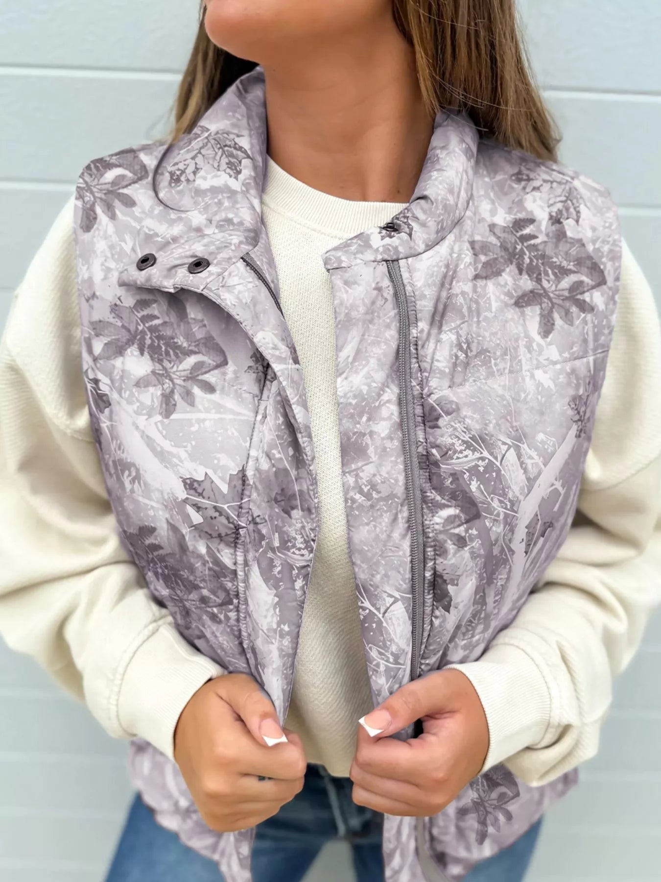 Gray sleeveless zip-up vest with leaf woodland camo print. Lightweight, unlined body, casual fit for outdoor days and easy outfits with denim or hoodies.