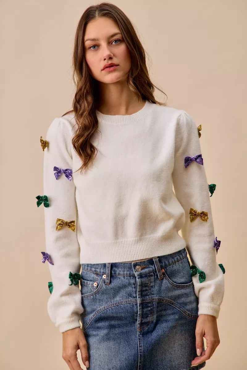 Ivory women’s knit sweater top with colorful glitter ribbon bows, lightweight casual-dressy fit, festive sparkle detail for everyday and seasonal outfits.
