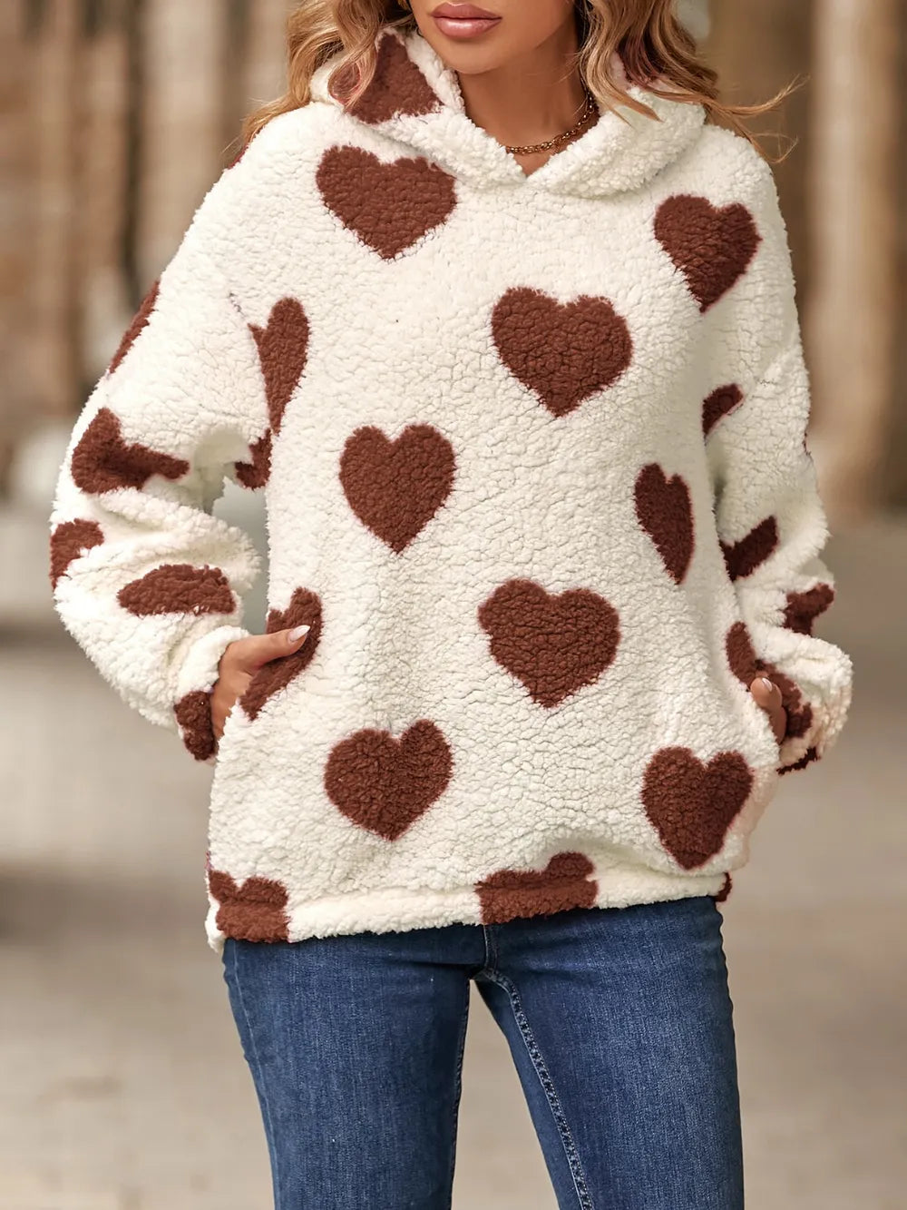 Fuzzy sherpa hoodie in off-white with brown heart-shaped pockets. Long sleeves, dropped shoulder pullover fit, soft cozy casual look.
