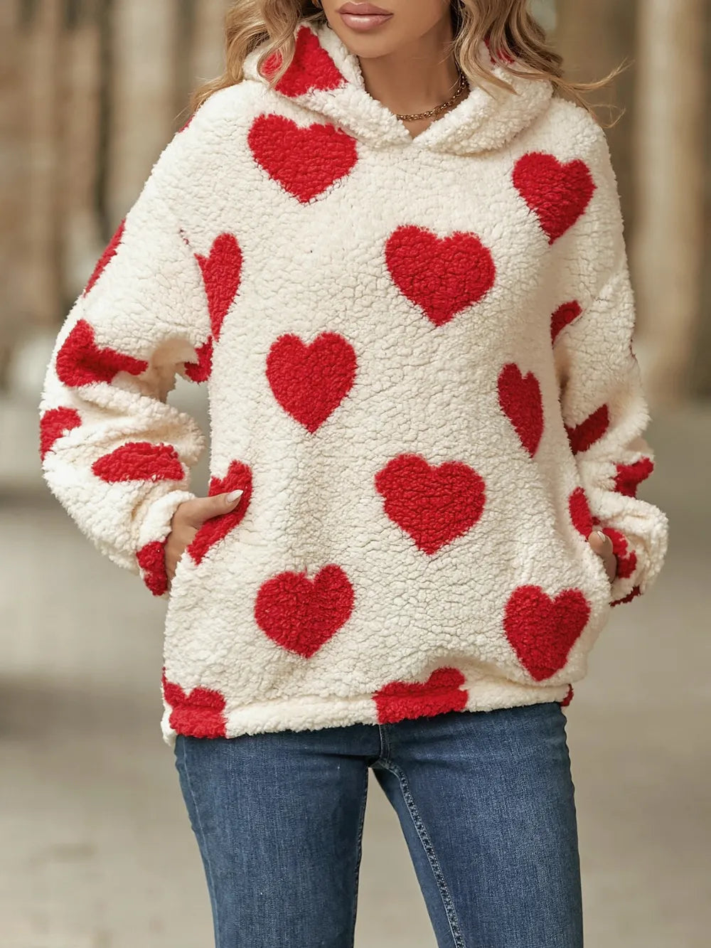Fuzzy sherpa hoodie in off-white with red heart-shaped pockets. Long sleeves, dropped shoulder pullover fit, soft cozy casual look.