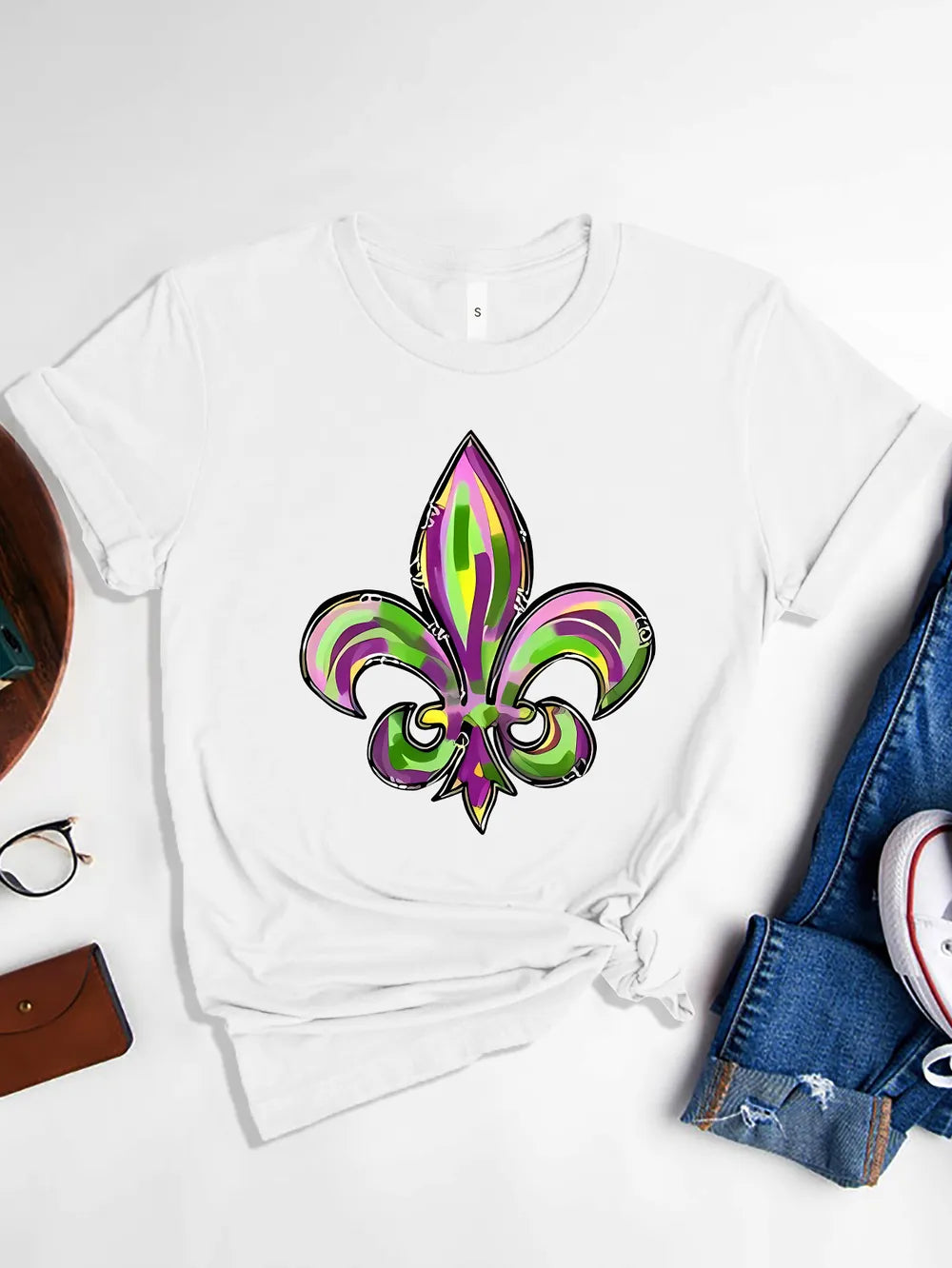 White graphic tee with purple, green & gold fleur-de-lis Mardi Gras design. Soft stretch fit for parade season and everyday festive styling.