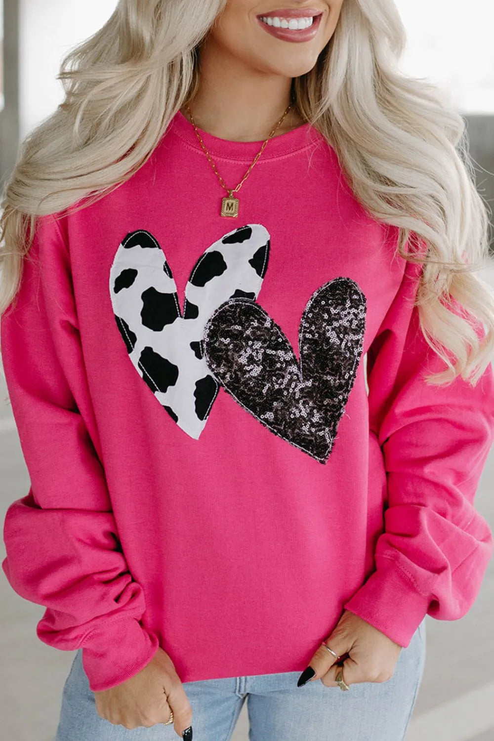Pink sweatshirt with cowprint heart patch and black sequin heart stitched on. Opaque fabric, relaxed pullover fit, long sleeves, casual outfit favorite.